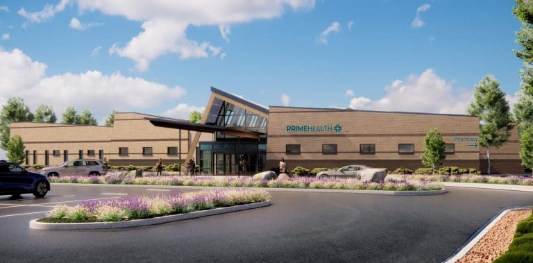 A modern medical building labeled PRIME HEALTH with large windows and landscaped flower beds in the parking lot, several cars, and a few people walking toward the entrance under a partly cloudy sky, representing quality healthcare in Grand Junction.