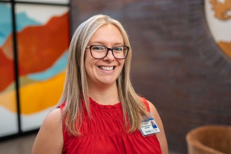jessica boff primehealth plus grand junction colorado blonde woman with glasses and red shirt stands in front of colorful background